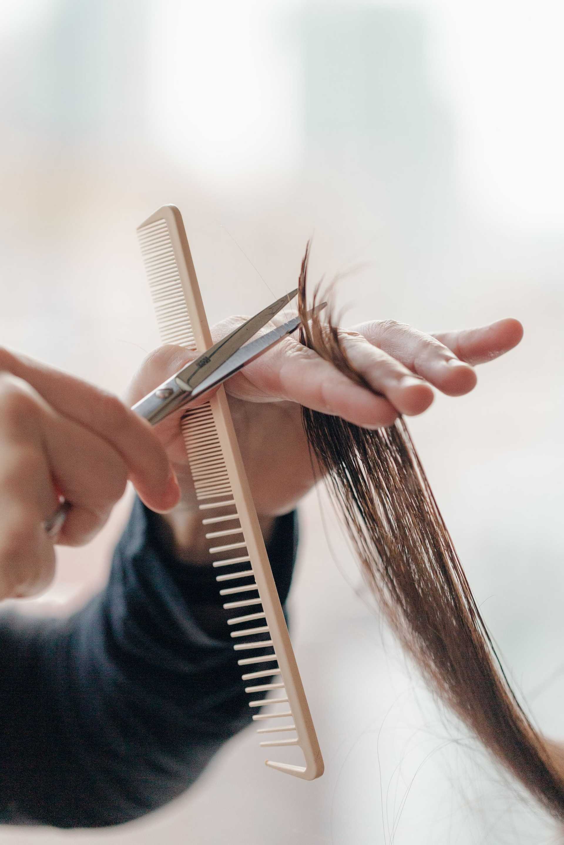 Close-up of a hand cutting a person's brown hair with scissors and a comb.