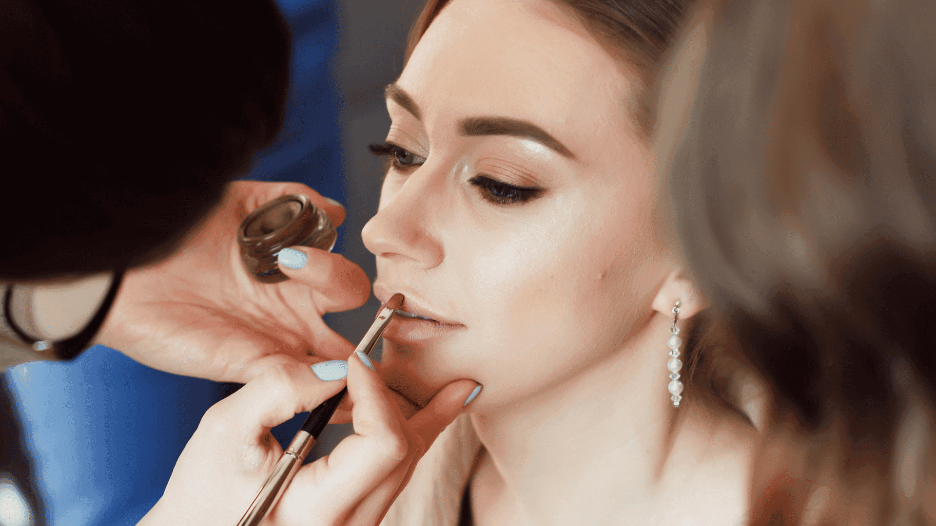 Makeup artist applying lipstick to a woman with focus on her lips and hand holding the brush.