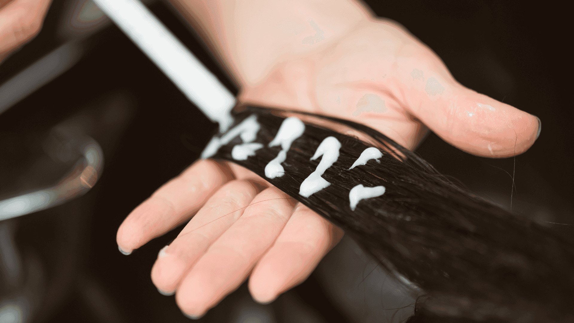 Hair treatment being applied to dark brown hair held in hand.